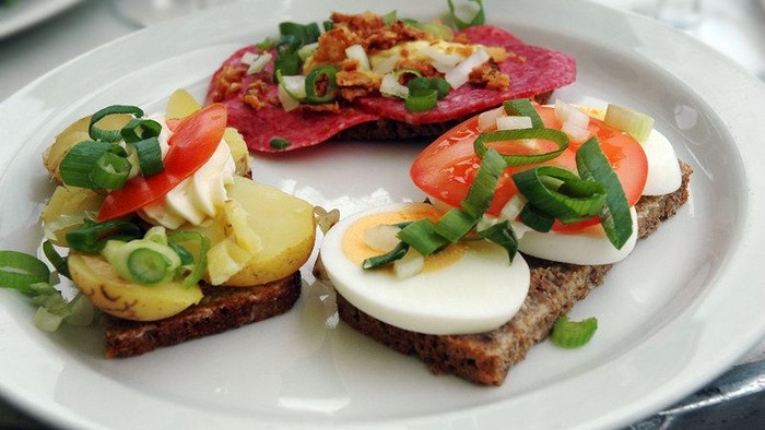 En ret med tre brødskiver med æg, tomater og grønne løg.