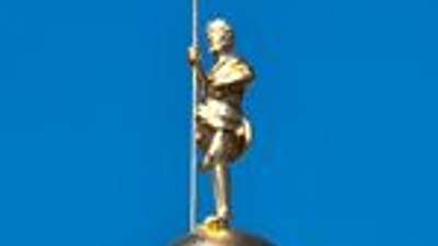 En spiraltrappetårn kronet med en gylden kugle og kors mod en klar blå himmel.