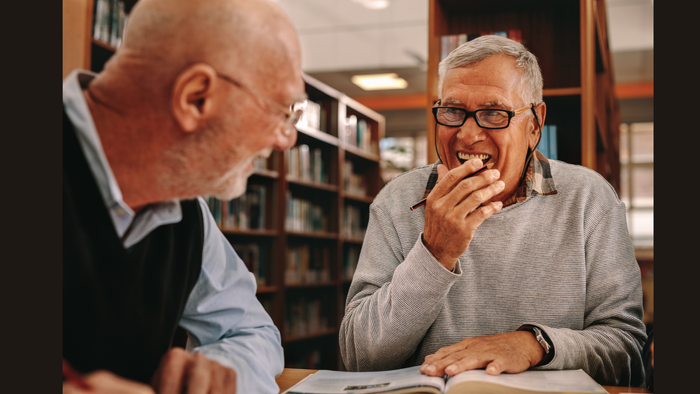 Zwei ältere Männer sitzen in einer Bibliothek und unterhalten sich.
