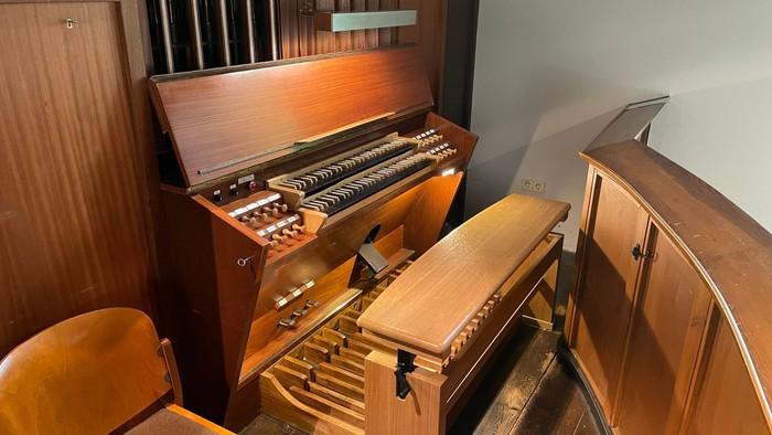 Ein hölzernes Harmonium mit geöffneten Registern und einem Stuhl davor