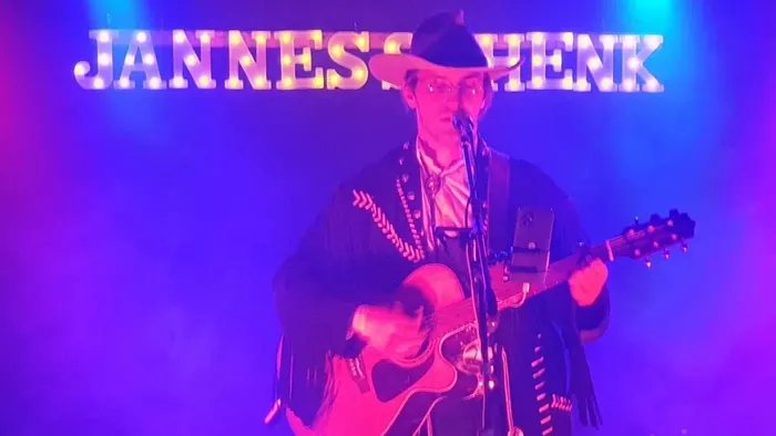 Ein Mann spielt auf einer Bühne unter blauen Lichtern und einem beleuchteten Schild Gitarre