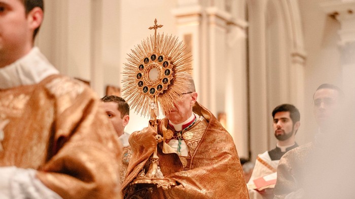 Ein Priester führt eine Prozession in einer Kirche an, trägt eine Monstranz mit dem Allerheiligsten.