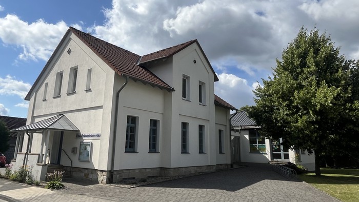 Das Bild zeigt das Laggenbecker Gemeindehaus, ein weiß verputztes Gebäude mit einem Anbau rechts.