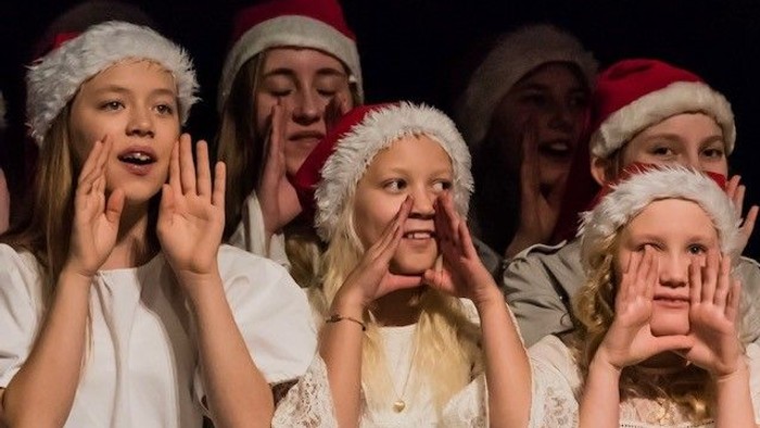 Fire piger i julehatter og hvide skjorter, der smiler og holder hænderne op for øjnene.