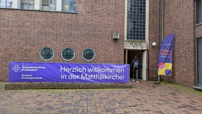 Vor einem Backsteingebäude steht ein Banner mit der Aufschrift