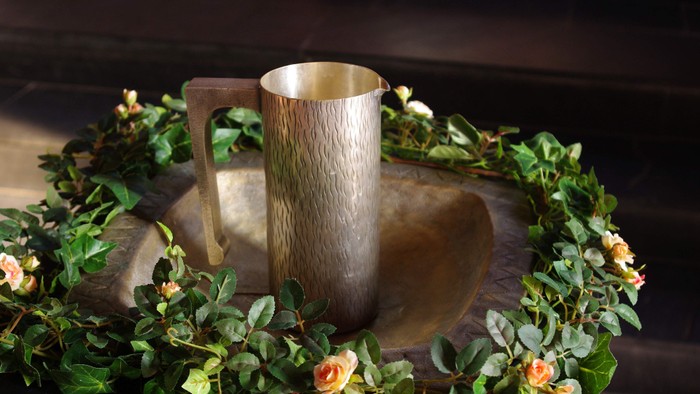 Taufbecken mit Wasserkanne und grünem Blumenkranz