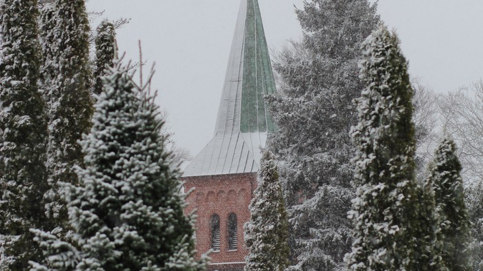 Snefaldende skove med kirke i baggrunden