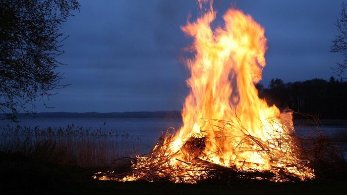 Ein großes Lagerfeuer brennt am Ufer eines Sees bei Dämmerung