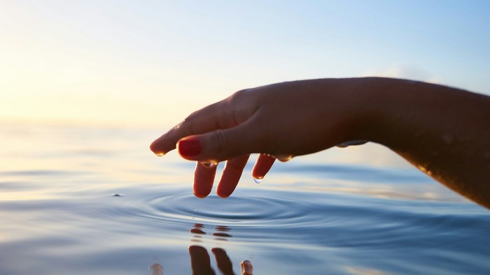 Hand berührt Wasser bei Sonnenuntergang.