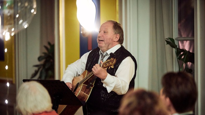 En mand spiller guitar og synger i et rum med gæster.