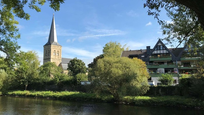 Ein ruhiger Fluss mit Kirche und Häusern im Hintergrund