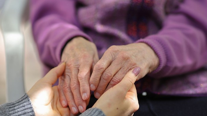 En ung person holder en ældre persons hænder i trøst.