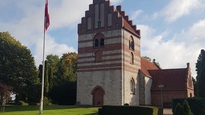 En smuk middelalderlig kirke med tårn og flagstang i en parkagtig omgivelse