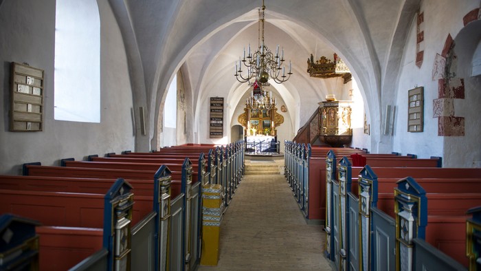 Indre del af kirke med høje buegange og røde bænke.