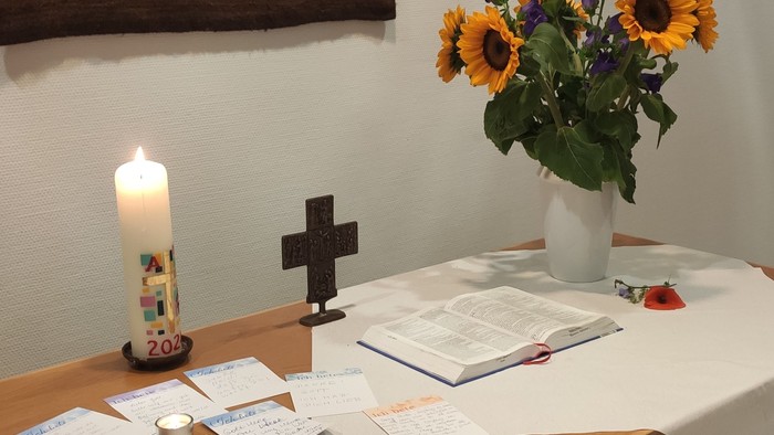 Ein Tisch mit Kerze, Kreuz und Blumen in einem Raum