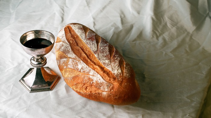 Loaf of bread and chalice with wine on white cloth