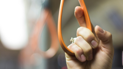 Eine Hand hält ein orangefarbenes Gummibandarmband mit einem kleinen weißen Blütenanhänger.