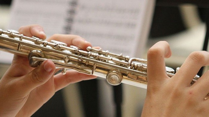 Hænder, der spiller på en fløjte med noder synlige i baggrunden.