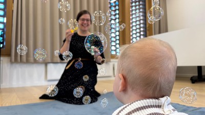 Baby og underviser deltager i babysalmesang med sæbebobler