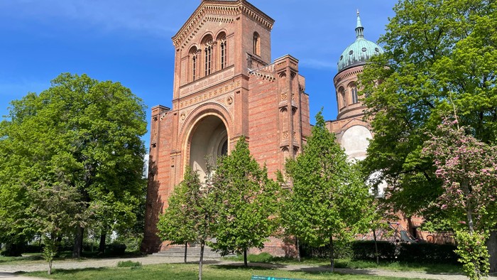 Große rote Backsteinkirche mit grünem Turm und Parkbank im Vordergrund