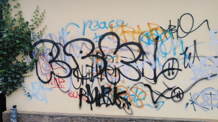 Graffiti an beigen Wand mit Bäumen und Ziegelmauer