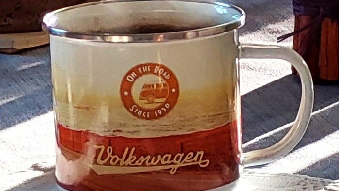 Ein VW-Becher mit dampfendem Kaffee auf einem Tisch.