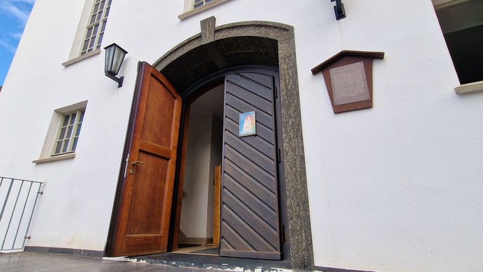 Das Bild zeigt einen Hauseingang mit zwei geöffneten Holztüren und einer weißen Fassade.