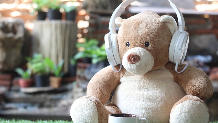 En teddybear med hodetelefoner sidder med en kaffekop på græs.
