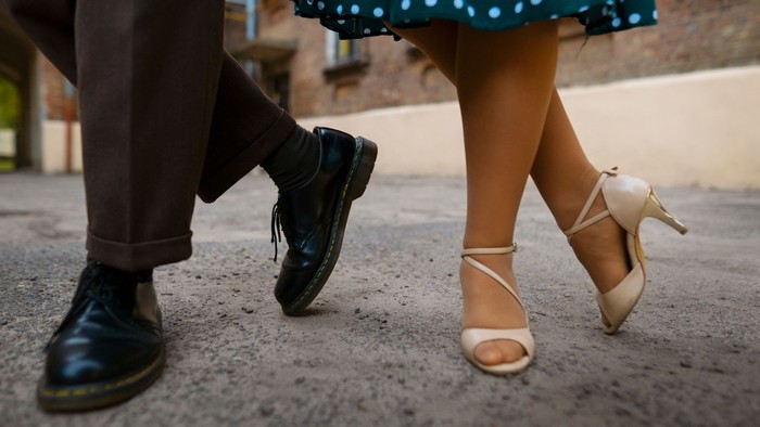 Zwei Personen tanzen, eine mit schwarzen Schuhen, die andere mit High Heels.