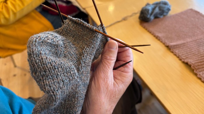 En person sitter og stråler en grå strømpe med nåler.