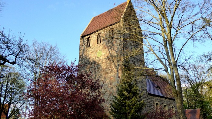 Alte Kirche mit hohem Turm und rotem Dach, umgeben von Bäumen und Büschen