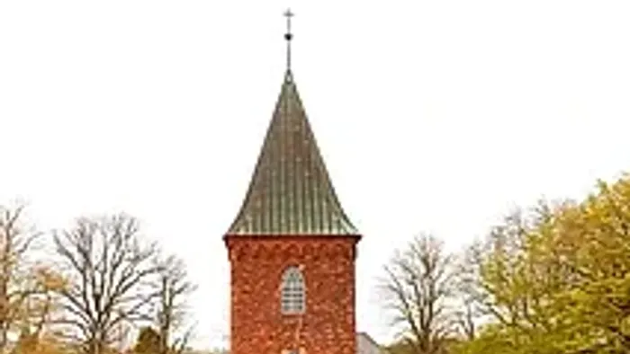 Kleine rote Kirche mit hohem Turm in parkähnlichem Garten.