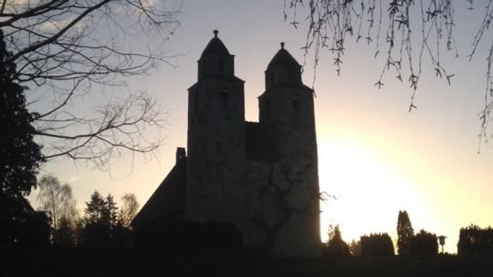 En middelalderlig kirke mod solnedgang med træer i forgrunden