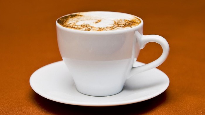 Eine weiße Tasse mit Kaffee und Milchschaum auf Untertasse.