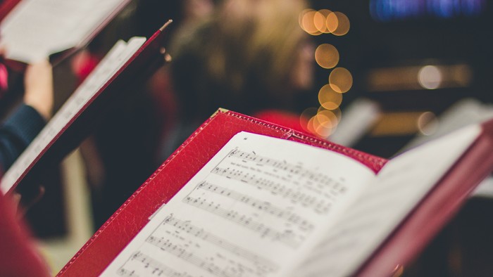 A red book with musical notes and a pencil, blurry background with people.