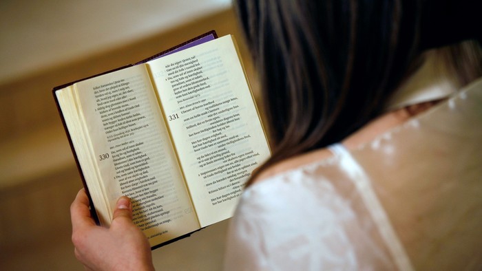 En person læser en åben bog med tekst på begge sider iført et lysefarvet tøjstykke.