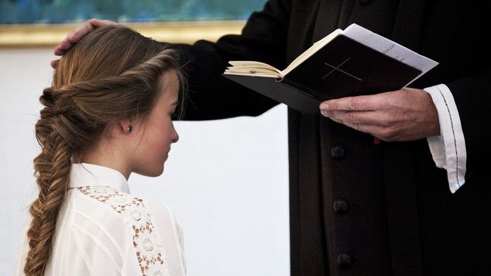 En kvinde med frisyr og hvid blouse ser op på en bog holdt af en mand i mørkt tøj.