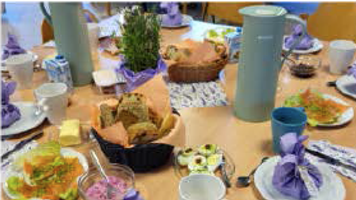 Ein Tisch mit verschiedenen Gerichten, Tellern und Getränken, inklusive einer Teekanne und einer Vase mit lila Blumen.