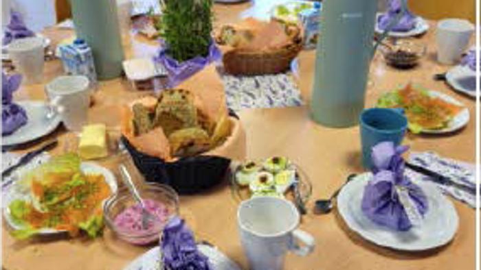 Ein Tisch mit verschiedenen Gerichten, Tellern und Getränken, inklusive einer Teekanne und einer Vase mit lila Blumen.