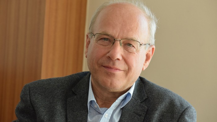 Ein älterer Mann mit Brille und Anzug lächelt in die Kamera.