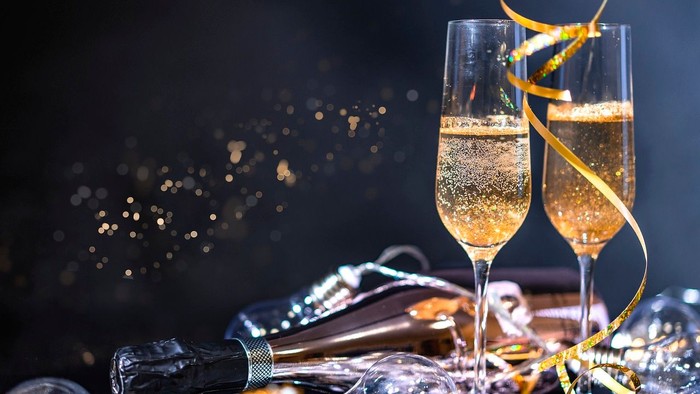 To flåsklasser med skummet champagne og guldstjerner i mørkt miljø