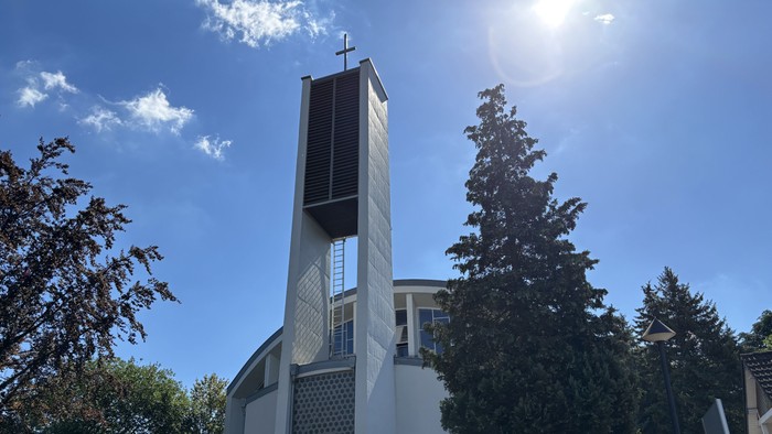 Moderne Kirche mit hohem Glockenturm vor strahlend blauem Himmel und umgeben von Grün.