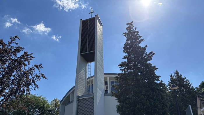 Moderne Kirche mit hohem Glockenturm vor strahlend blauem Himmel und umgeben von Grün.
