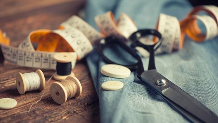 Nähutensilien wie Schere, Maßband und Nadeln auf Holzplatte