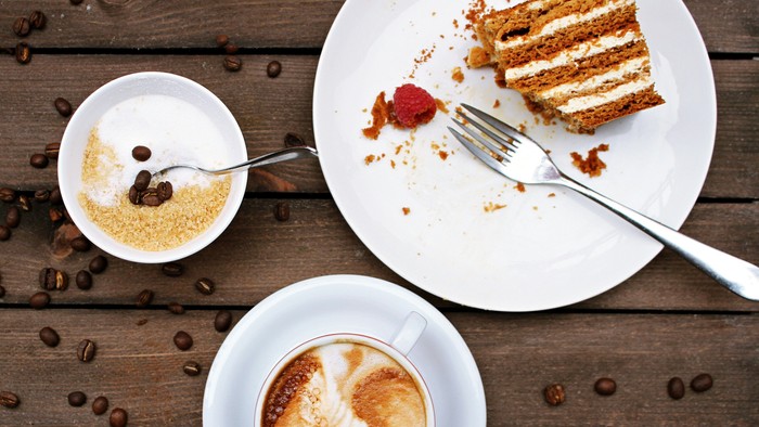 Ein Stück Kuchen, eine Tasse Kaffee und eine kleine Schale mit Zucker auf einem Holztisch