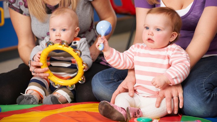 Zwei Babys spielen mit Musikinstrumenten, während Erwachsene sie unterstützen