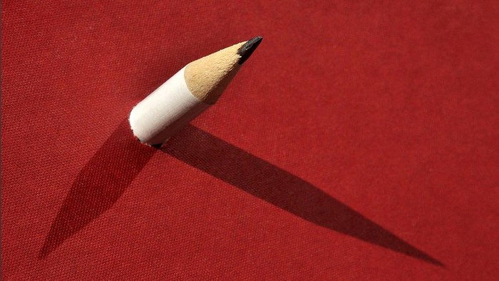 Gespritzter Bleistift ragt aus rotem Stoff und wirft scharfe Schatten