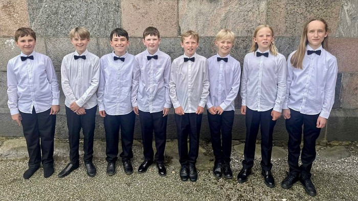 En gruppe drenge i formelle klæder står foran en mur