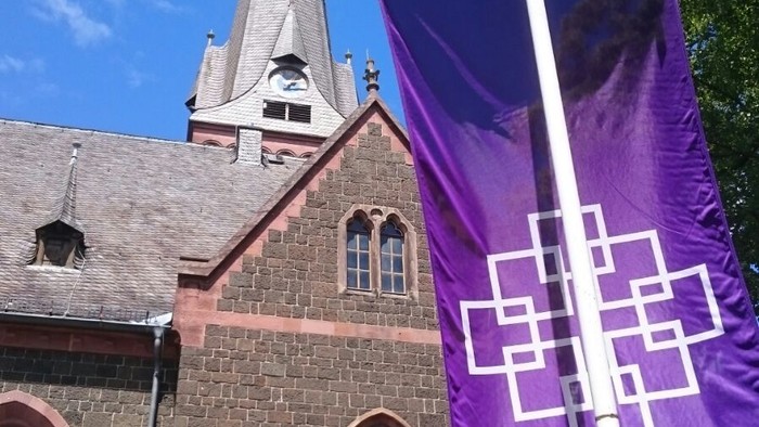 Purpurbanner vor gotischer Kirche mit hohem Turm und spitzen Dach