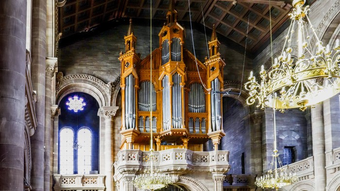 Orgue en bois doré suspendu dans une église avec vitraux et lustres.